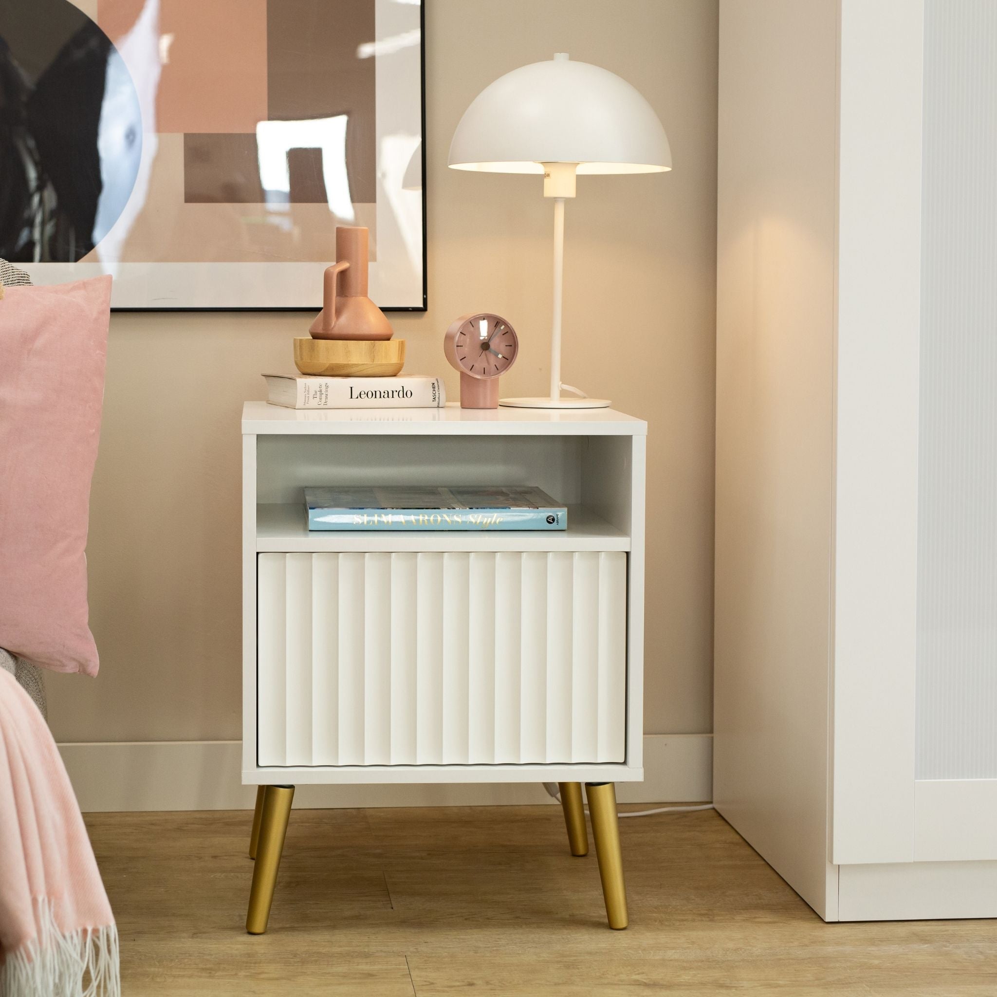 Balta Barcelona naktinė spintelė su stalčiumi, dekoruota knygomis, laikrodžiu ir stalinės lempos interjere